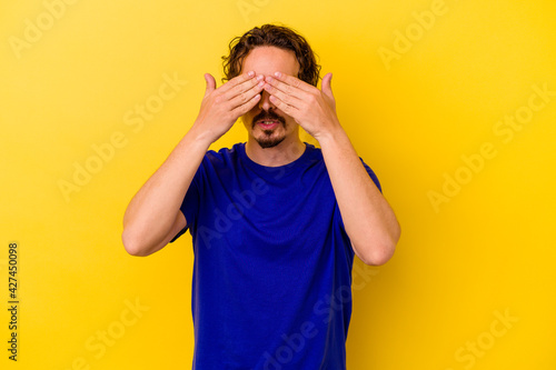 Young caucasian man isolated on yellow background afraid covering eyes with hands.