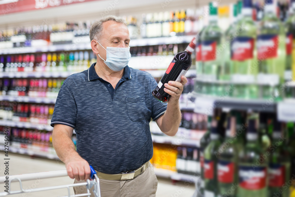 Man in protective mask buying bottle of wine in store with alcohol drinks