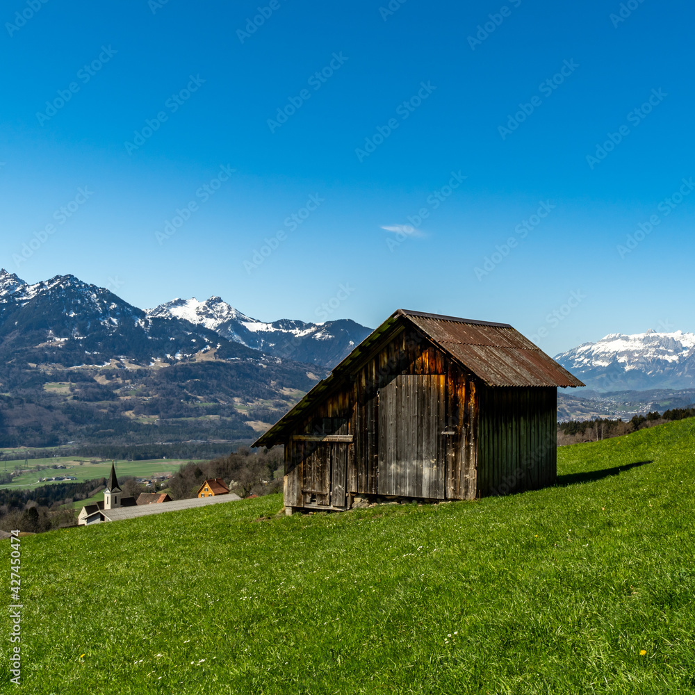 Eine alte Holzscheune, Heuschober oder Stadel in Düns, im Grossen Walsertal, mit Blick zum Rhätikon, Alpstein und Säntis. blauer Himmel und verschneite Bergspitzen.