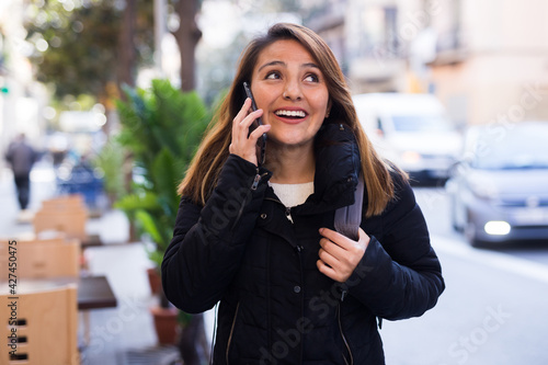 Happy girl talking on phone while walking along city street