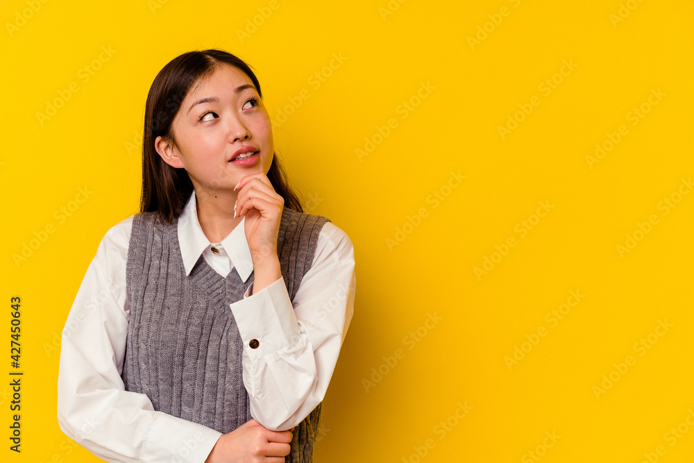 Young chinese woman isolated on yellow background relaxed thinking about something looking at a copy space. Young chinese woman isolated on yellow background relaxed thinking about something looking at a copy space.