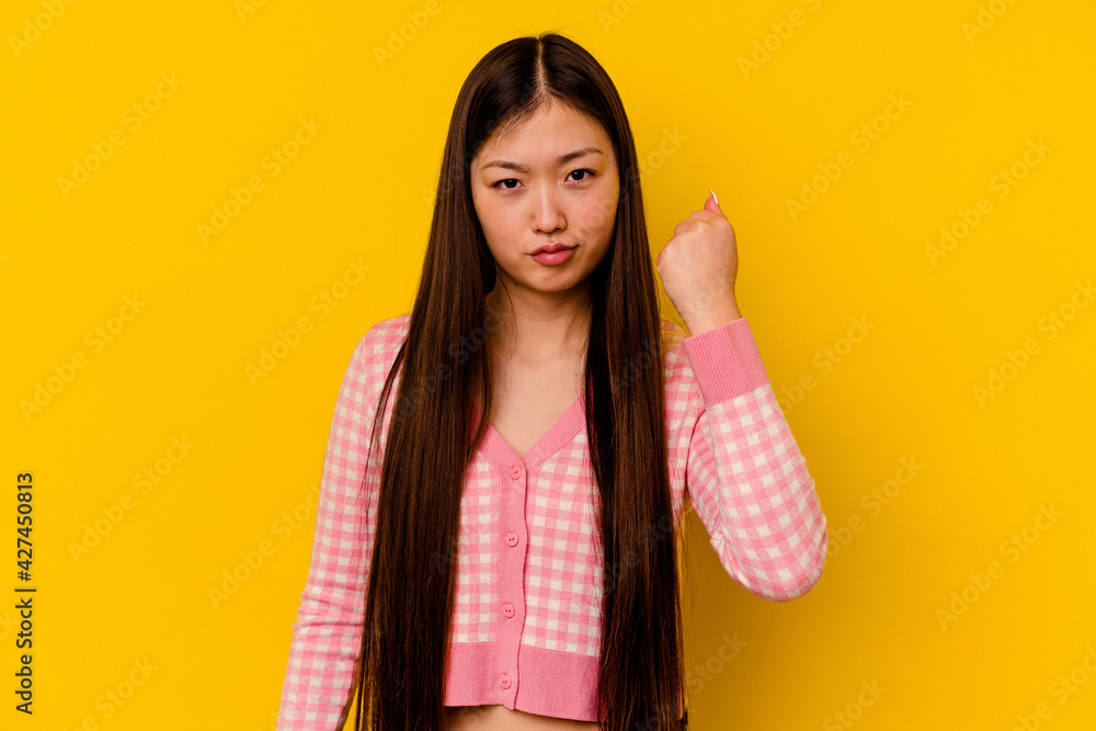 Young chinese woman isolated on yellow background showing fist to camera, aggressive facial expression. Young chinese woman isolated on yellow background showing fist to camera, aggressive facial expression.