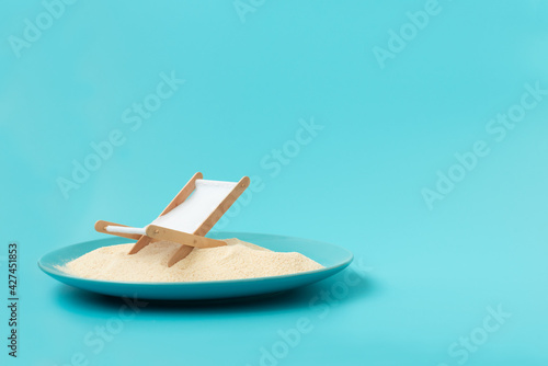 Tropical beach concept made of plate with sand, deck chair and sun umbrella. Creative summer vacation concept