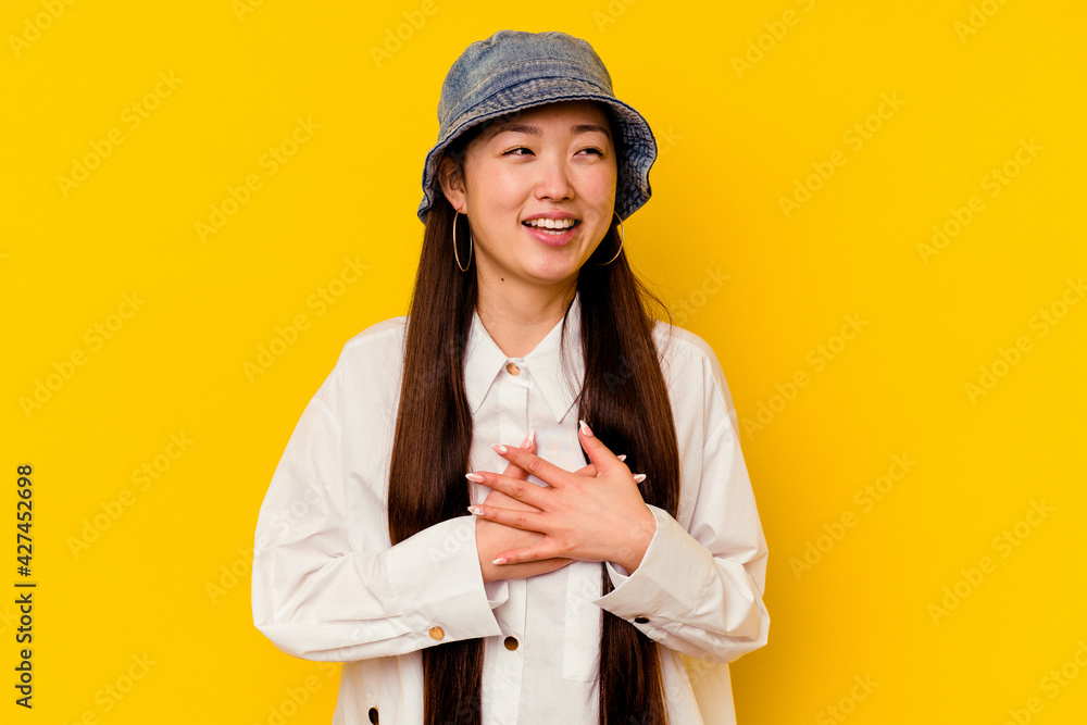 Young chinese woman isolated on yellow background laughing keeping hands on heart, concept of happiness. Young chinese woman isolated on yellow background laughing keeping hands on heart, concept of happiness.