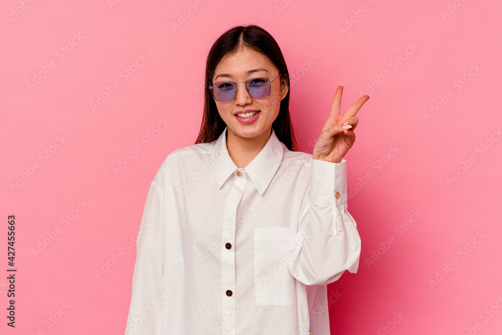 Young chinese woman isolated on pink background joyful and carefree showing a peace symbol with fingers. Young chinese woman isolated on pink background joyful and carefree showing a peace symbol with fingers.