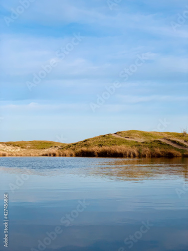 Lake view with grassy, warm hills in the background , reflecting on the water