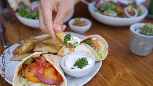 Healthy plant based lunch of wraps and potatoes on a side. Hand dipping a potato wing in the vegan mayo sauce. 