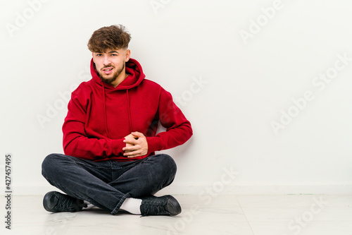 Young Moroccan man sitting on the floor isolated on white background having a liver pain, stomach ache. © Asier
