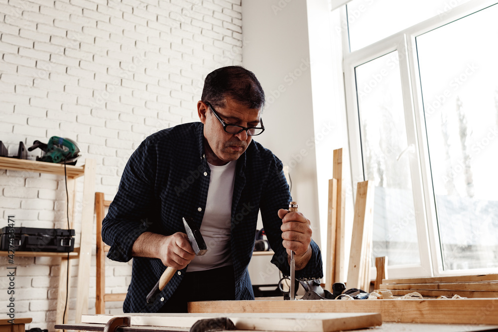 Middle-aged man carpenter working in a workshop with chisel and hammer Middle-aged man carpenter working in a workshop with chisel and hammer