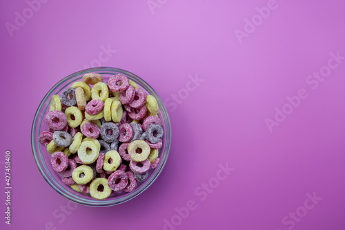 Sweet multicolored flakes in the form of a ring in a round bowl on a pink background