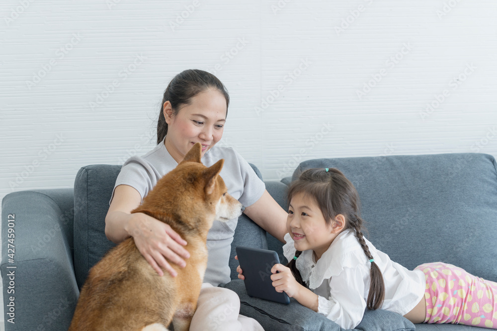 © Thirawatana - A mom and daughter is using a tablet computer and has a Shiba Inu on the sofa. Mom and baby.