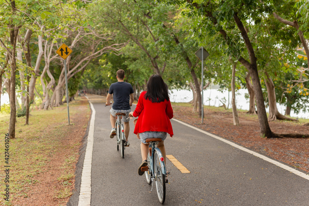 Back view of couple riding bicycles in the park.