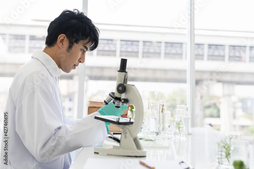 Asian man scientists tests of plants with microscope and glassware in laboratory. Scientists doing analysis for germs and bacteria in the laboratory. Researcher and discovery concept