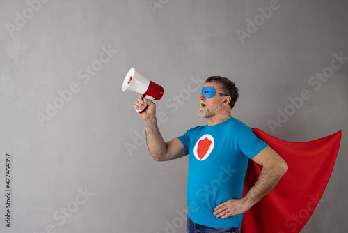 Senior man wearing superhero costume shouting through loudspeaker