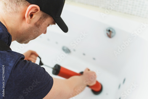 Plumber unclogging bathtub with professional force pump cleaner.