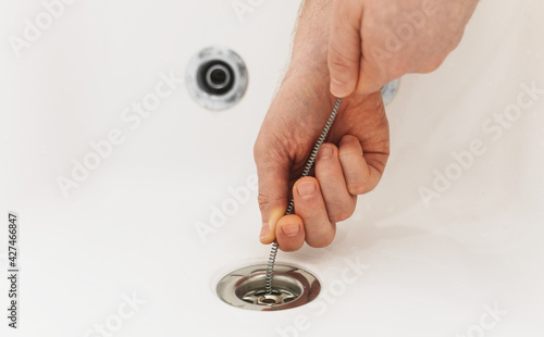 Plumber using drain snake to unclog bathtub.