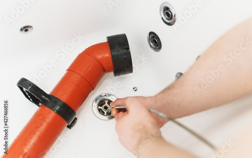 Plumber using drain snake to unclog bathtub.