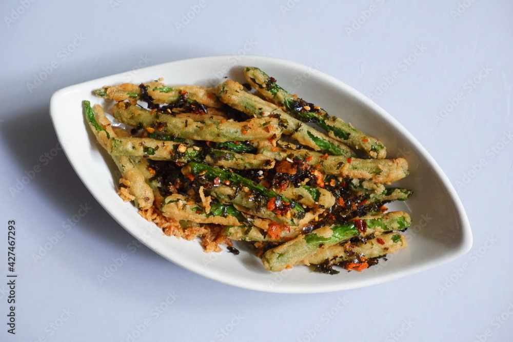 a plate of fried crispy green beans served with chili flakes in white background a plate of fried crispy green beans served with chili flakes in white background