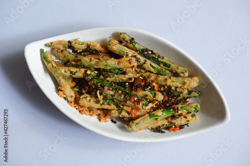 a plate of fried crispy green beans served with chili flakes in white background