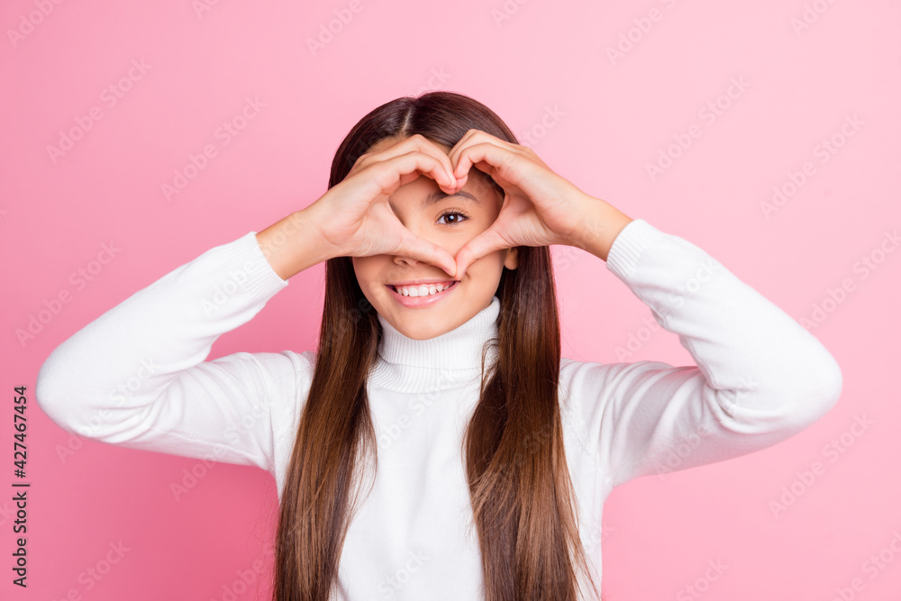 Photo of adorable cheerful girl arms fingers show heart symbol near eye isolated on pink color background Photo of adorable cheerful girl arms fingers show heart symbol near eye isolated on pink color background