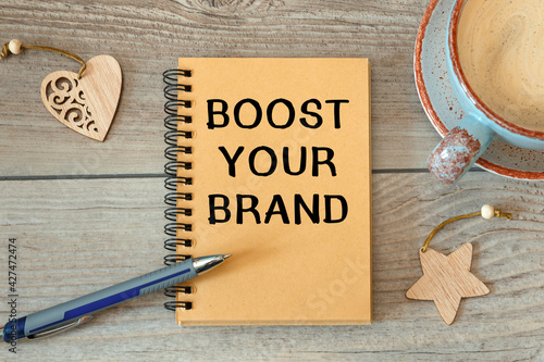 BOOST YOUR BRAND - inscription on a notebook and cup with coffee.