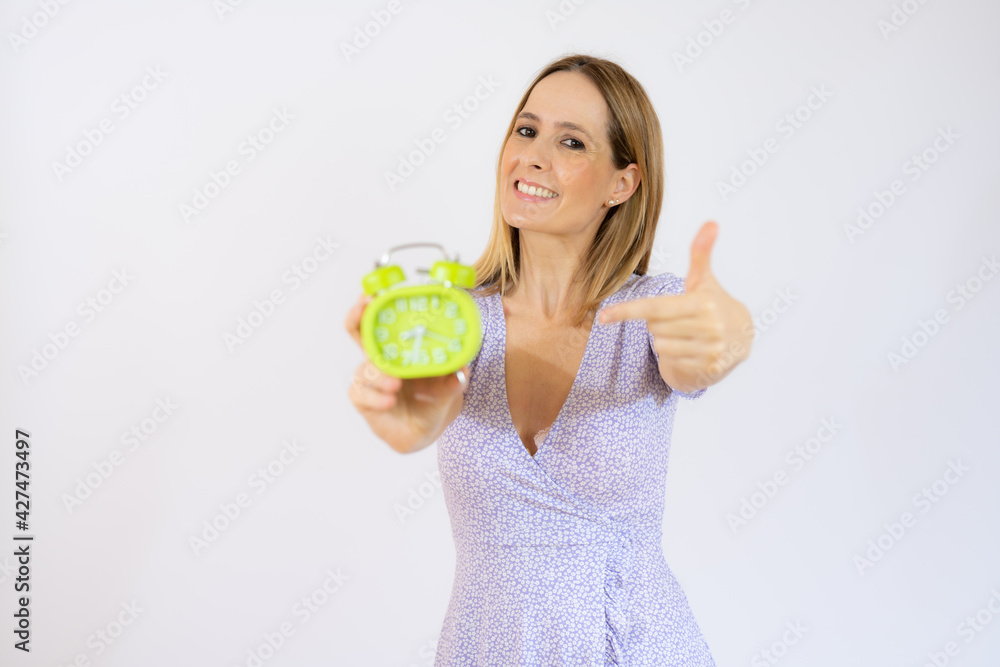 Young beautiful woman holding alarm clock standing over isolated white background with happy face smiling Young beautiful woman holding alarm clock standing over isolated white background with happy face smiling