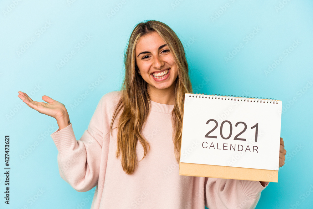 Young blonde caucasian woman holing a calendar isolated showing a copy space on a palm and holding another hand on waist. Young blonde caucasian woman holing a calendar isolated showing a copy space on a palm and holding another hand on waist.