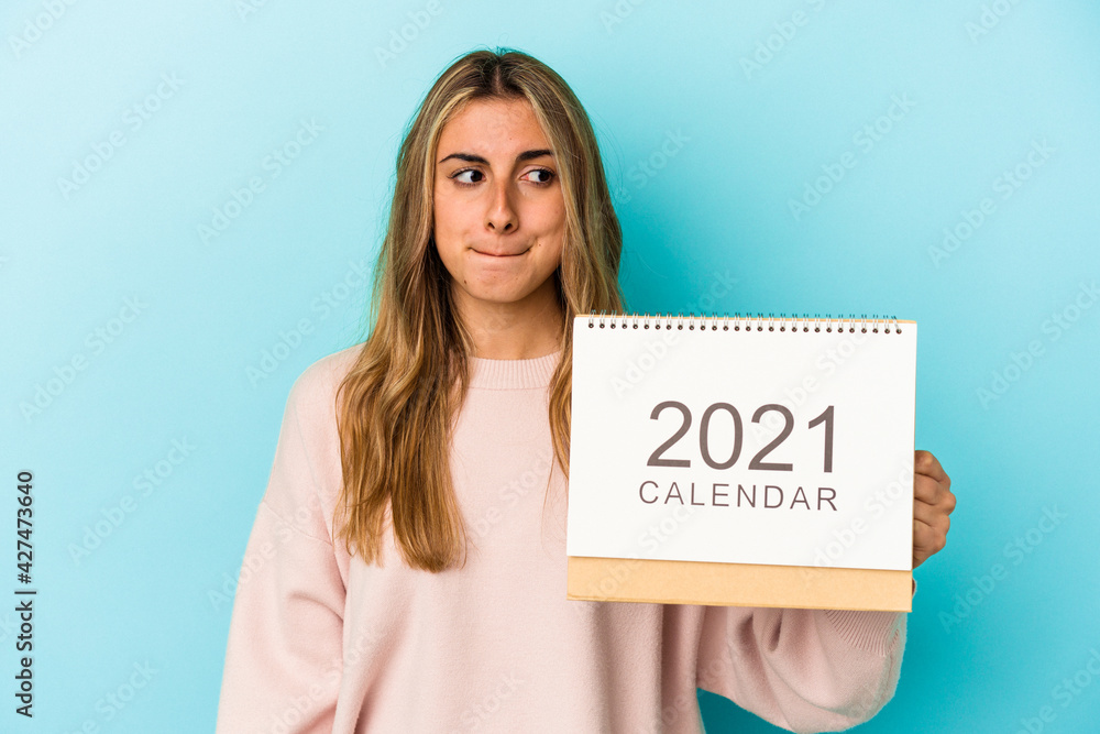 Young blonde caucasian woman holing a calendar isolated confused, feels doubtful and unsure. Young blonde caucasian woman holing a calendar isolated confused, feels doubtful and unsure.