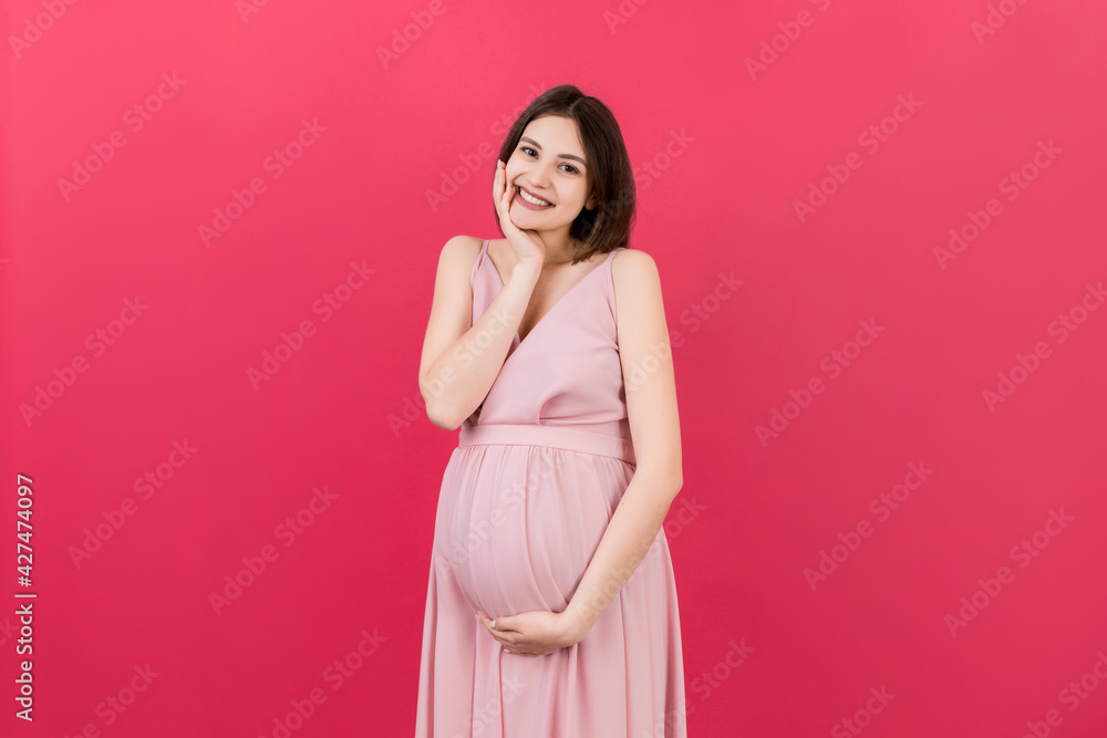 Happy pregnant woman touching her abdomen at Colored background. Future mother is wearing white underwear. Expecting of a baby. Copy space Happy pregnant woman touching her abdomen at Colored background. Future mother is wearing white underwear. Expecting of a baby. Copy space