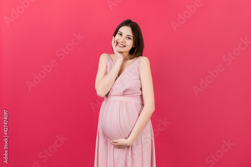 Happy pregnant woman touching her abdomen at Colored background. Future mother is wearing white underwear. Expecting of a baby. Copy space