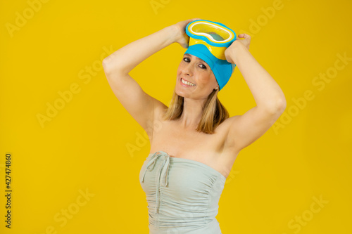 Smiling young woman wearing swimsuit and diving goggles isolated over yellow background