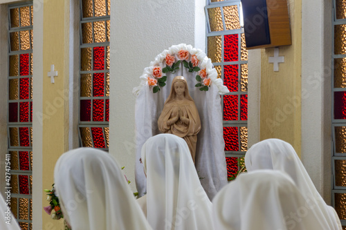 Veiled heads of nuns praying and singing before an image of the Virgin Mary in a flowered niche in the chapel. Convent of the Servants of the Eucharist, Ponta Grossa City, Parana State, Brazil.