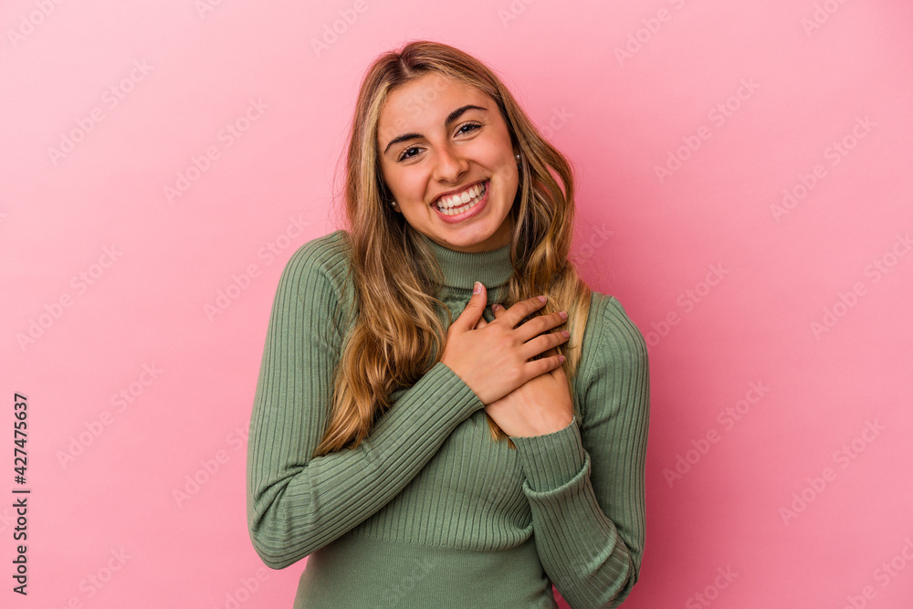 Young blonde caucasian woman isolated on pink background laughing keeping hands on heart, concept of happiness. Young blonde caucasian woman isolated on pink background laughing keeping hands on heart, concept of happiness.
