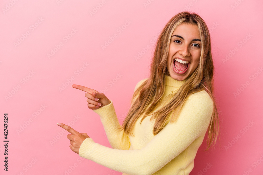 Young blonde caucasian woman isolated on pink background excited pointing with forefingers away. Young blonde caucasian woman isolated on pink background excited pointing with forefingers away.