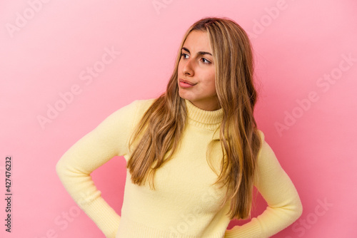 Young blonde caucasian woman isolated on pink background looks aside smiling, cheerful and pleasant.