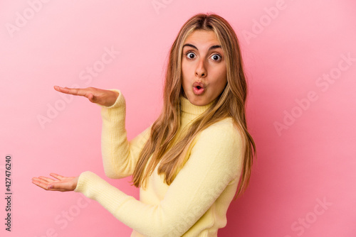 Young blonde caucasian woman isolated on pink background holding something with both hands, product presentation.