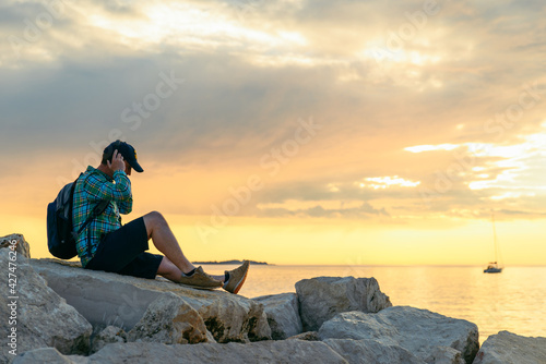 man with backpack looking on sunset over the sea listening music