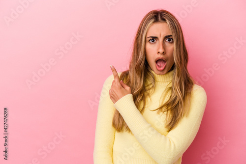 Young blonde caucasian woman isolated on pink background pointing to the side
