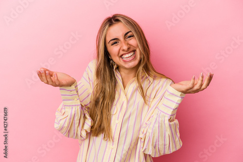 Young blonde caucasian woman isolated on pink background makes scale with arms, feels happy and confident.