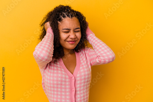 Young african american woman isolated on yellow background covering ears with hands. © Asier