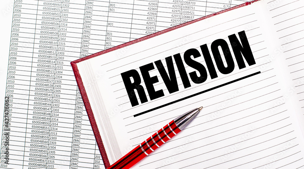 On the table next to the reports is a diary with the text REVISION. Nearby is a red handle. On the table next to the reports is a diary with the text REVISION. Nearby is a red handle.