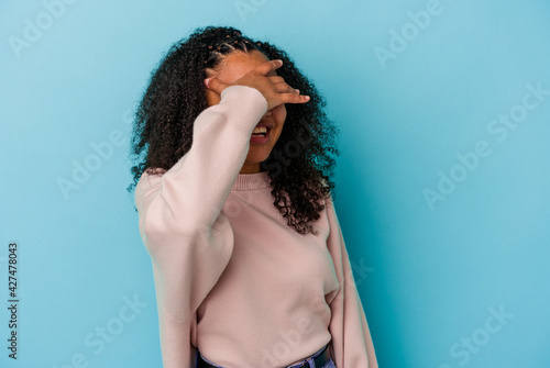 Young african american woman isolated on blue background covers eyes with hands, smiles broadly waiting for a surprise.