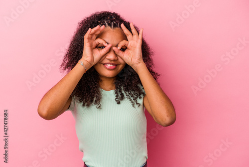 Young african american woman isolated on pink background showing okay sign over eyes