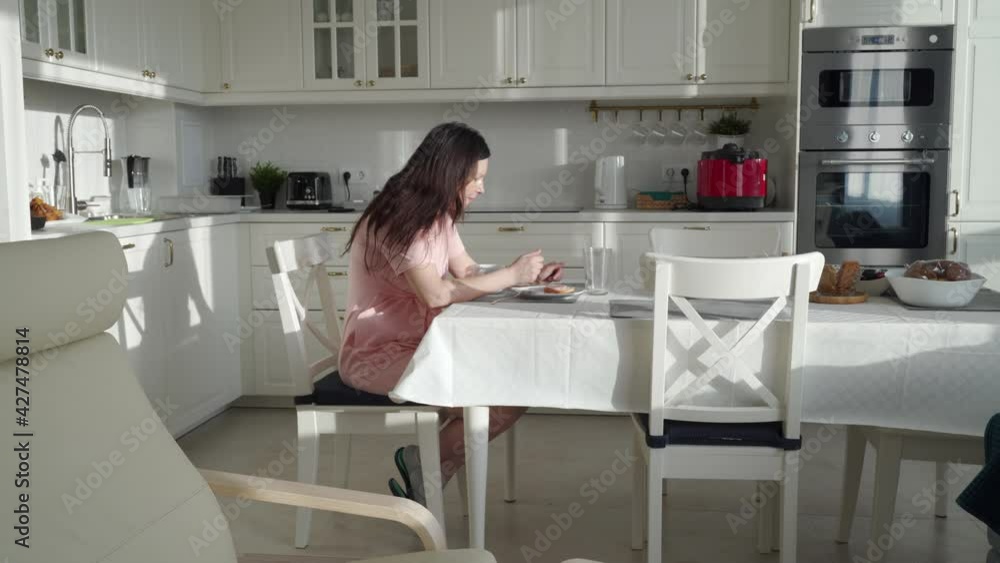 Woman eating breakfast using smartphone in open plan kitchen living room on sunny morning. High quality 4k footage Woman eating breakfast using smartphone in open plan kitchen living room on sunny morning. High quality 4k footage