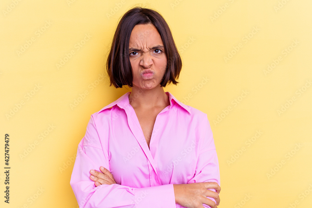 Young mixed race woman isolated on yellow background frowning face in displeasure, keeps arms folded. Young mixed race woman isolated on yellow background frowning face in displeasure, keeps arms folded.