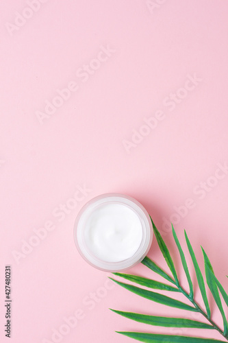 Jar of cosmetic cream with leaf palm branch on pink background. Flat lay  copy space