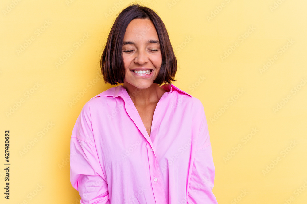 Fototapeta premium Young mixed race woman isolated on yellow background laughs and closes eyes, feels relaxed and happy.