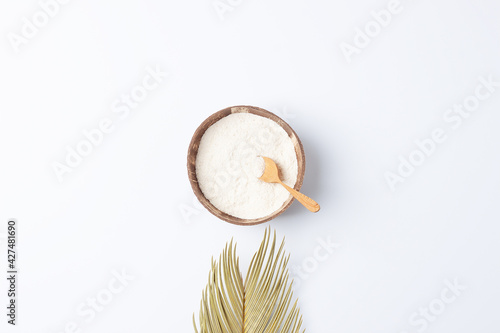 Collagen powder in bowl with measure spoon with palm leaves on white background. Flat lay, copy space