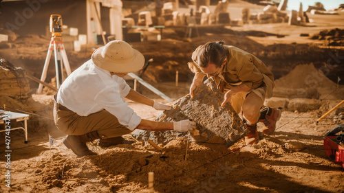 Archaeological Digging Site: Two Great Archeologists Work on Excavation Site, Carefully Cleaning, Lifting Newly Discovered Ancient Civilization Cultural Artifact, Historic Clay Tablet, Fossil Remains photo