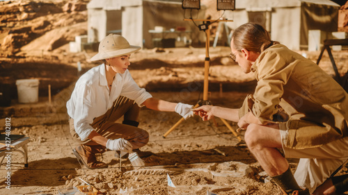 Archaeological Digging Site: Two Great Paleontologists Discovered Fossil Remains of Prehistoric Dinosaur, Passing Fragment to each Other. Archeologists Work on Excavation Site, Discover Species Bones